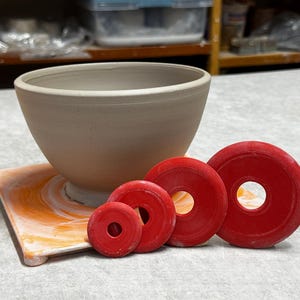 May include: Four red ceramic rings of different sizes with a white ceramic bowl on a square orange and white tile.