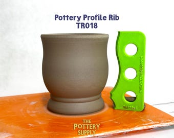 May include: A pottery profile rib and a ceramic mug. The mug is a light brown color with a rounded shape. The green rib has three holes and the text "THE POTTERY SUPPLY". The text "Pottery Profile Rib TR018" is also visible.
