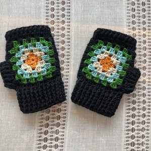 Puede incluir: Un par de guantes sin dedos de ganchillo negros con un diseño de cuadrado de la abuela verde, azul y naranja.