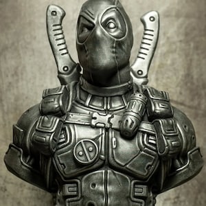 Puede incluir: Busto gris metálico del personaje Deadpool de Marvel Comics. El busto presenta una máscara detallada, dos espadas en la espalda y un cinturón de herramientas con una granada. La figura está esculpida con intrincados detalles de armadura.