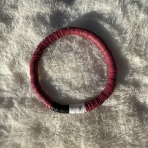May include: A burgundy, black, and white beaded bracelet. The bracelet is made of round, flat beads that are stacked on top of each other.