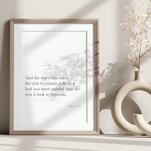 May include: A framed print featuring a quote about the risk of staying in a bud versus the risk of blossoming. The quote reads "And the day came when the risk to remain tight in a bud was more painful than the risk it took to blossom." The quote is attributed to "Anne Lamott".