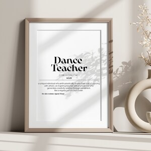 Könnte beinhalten: Ein gerahmter Druck mit weißem Hintergrund und schwarzem Text, der "Dance Teacher" lautet und eine Definition des Wortes enthält. Der Druck steht auf einem weißen Regal mit einer Vase und getrockneten Blumen.