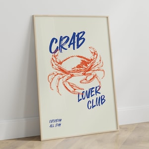 Op de afbeelding: Een ingelijste poster met een witte achtergrond en een rode krabillustratie. De tekst "CRAB LOVER CLUB" is in blauw geschreven met een handschrift. De tekst "EVERYDAY ALL DAY" is in kleinere blauwe tekst onderaan de poster geschreven.