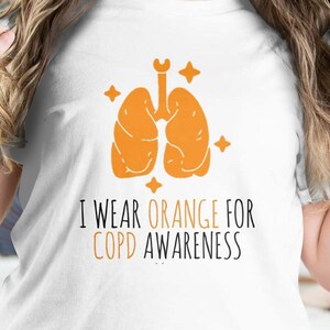 Puede incluir: Camiseta blanca con un gráfico de pulmón naranja y el texto "Uso naranja para la concienciación sobre la EPOC".