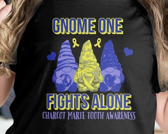 Può includere: T-shirt nera con la scritta "Gnome One Fights Alone" in giallo e bianco. La maglietta presenta tre illustrazioni di gnomi blu e gialli, con un simbolo a nastro. Il design promuove la consapevolezza della malattia di Charcot-Marie-Tooth.