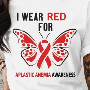 Può includere: Maglietta bianca con una farfalla rossa e il testo "Indossare il rosso per la consapevolezza dell'anemia aplastica".