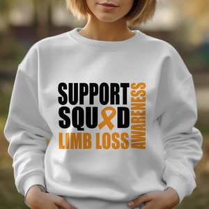 Puede incluir: Sudadera blanca con el texto "SUPPORT SQUAD LIMB LOSS AWARENESS" en negro y naranja. La palabra "SQUAD" tiene una cinta naranja en el medio.