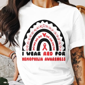 May include: White t-shirt with a black and red rainbow graphic and the text "I wear red for hemophilia awareness".