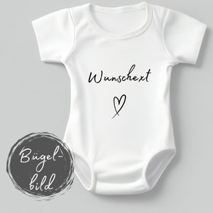 Könnte beinhalten: Weißer Baby Strampler mit schwarzem Text, der "Wunschext" mit einem Herzsymbol unter dem Text sagt. Der Strampler hat ein "Bügel-bild" Etikett in der linken unteren Ecke.