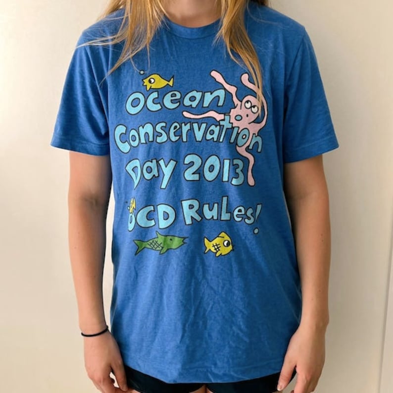 May include: A blue t-shirt with the text "Ocean Conservation Day 2013" and "OCD Rules!" printed on it. The shirt features a cartoon octopus and fish.