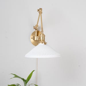 Puede incluir: Una pantalla de vidrio blanco con nervaduras con una pared de metal dorado ajustable. La pared tiene una cadena de tracción para encender y apagar la luz.
