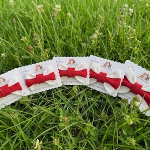 May include: Five pet bows with a cream base and a red centre bow, presented on white cards against green grass. The cards have text that reads "Pet Bow" and "Threaded Press".