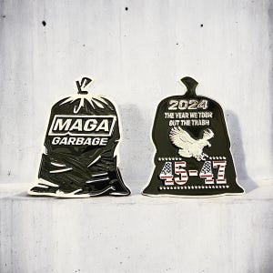 May include: Two black and gold garbage bag shaped pins. The first pin says "Maga Garbage". The second pin says "2024 The Year We Took Out The Trash 45-47".