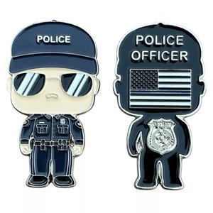 May include: Two silver-colored enamel pins depicting a cartoon police officer. The first pin shows a police officer with a blue hat that says "POLICE" on it, wearing sunglasses and a blue uniform. The second pin shows a police officer with a black hat that says "POLICE OFFICER" on it, with a thin blue line American flag and a silver badge.