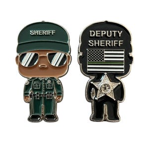 May include: Two enamel pins featuring a cartoon sheriff. The first pin is green and black and says "SHERIFF" on the hat. The second pin is black and white and says "DEPUTY SHERIFF" with a thin green line on the American flag.