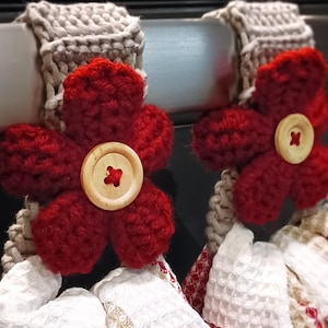Peut inclure: Deux porte-serviettes en crochet de fleurs rouges avec des boutons en bois accrochés à un support de cuisine argenté.