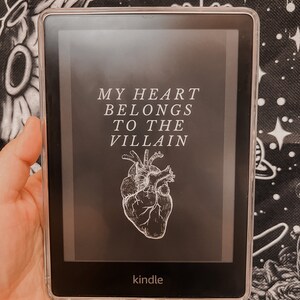May include: A Kindle e-reader displaying the title "My Heart Belongs to the Villain" with a stylised image of a heart.