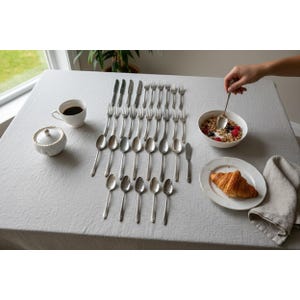 Può includere: Una tavola formale con posate, una tazza da tè bianca e una zuccheriera. Una ciotola di cereali con frutti di bosco, un croissant e un tovagliolo di lino sono anche sul tavolo. Una mano tiene un cucchiaio.