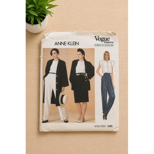 Op de afbeelding: Een Vogue Patterns naaipatroon-envelop voor Anne Klein-ontwerpen, genummerd 1385. De voorzijde bevat illustraties van drie outfits: een lange zwarte jas met een witte broek, een zwarte blazer met een bijpassende rok en een wit topje met een blauwe broek.