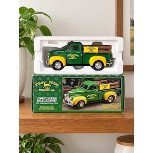 Könnte beinhalten: Ein grün-gelbes 1947 Studebaker Pickup-Modell aus Metalldruckguss mit John Deere Branding. Das Modell verfügt über eine braune Ladefläche in Holzoptik und befindet sich in einer weißen Styroporverpackung auf dem originalen grünen Karton.