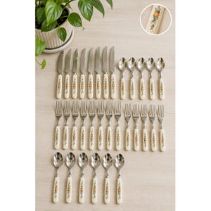 May include: A flatware set consisting of seven knives, seven forks, and six spoons, all featuring off-white handles decorated with a colorful fruit and leaf pattern. A circular inset shows a close-up of the handle design with an orange motif.