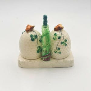 Może przedstawiać: Biały ceramiczny kubek z czarnym uchwytem i napisem "But First, Coffee" czarną, pogrubioną czcionką. Kubek stoi na białej powierzchni.