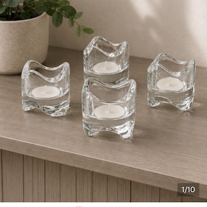 Peut inclure: Un ensemble de quatre bougeoirs chauffe-plat en verre transparent avec un bord ondulé et organique. Chaque bougeoir présente une base épaisse et une forme incurvée empilable, contenant une bougie chauffe-plat en cire blanche au centre.