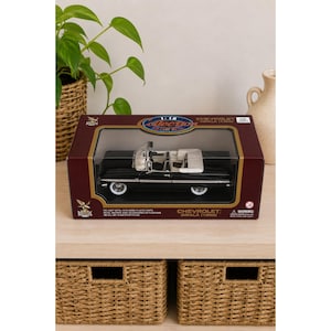 May include: A 1:18 scale die-cast metal model of a black 1959 Chevrolet Impala convertible with a white interior, housed in a rectangular display box. The box features the text 1:18 Collection, Chevrolet Impala 1959, and Die-Cast Metal.