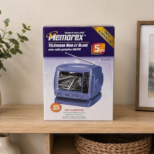 Peut inclure: Une boîte de marque Memorex pour un téléviseur noir et blanc avec radio AM/FM. La boîte est violette et blanche, présentant une image d'un téléviseur portable bleu avec une antenne, un écran affichant des rails et le texte 5 po.