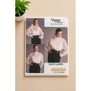 May include: A Vogue Patterns sewing pattern envelope for Ralph Lauren design 2001. The white paper envelope features three photographs of a sheer white long-sleeve blouse with a high collar, worn with a black belt and black skirt or trousers.