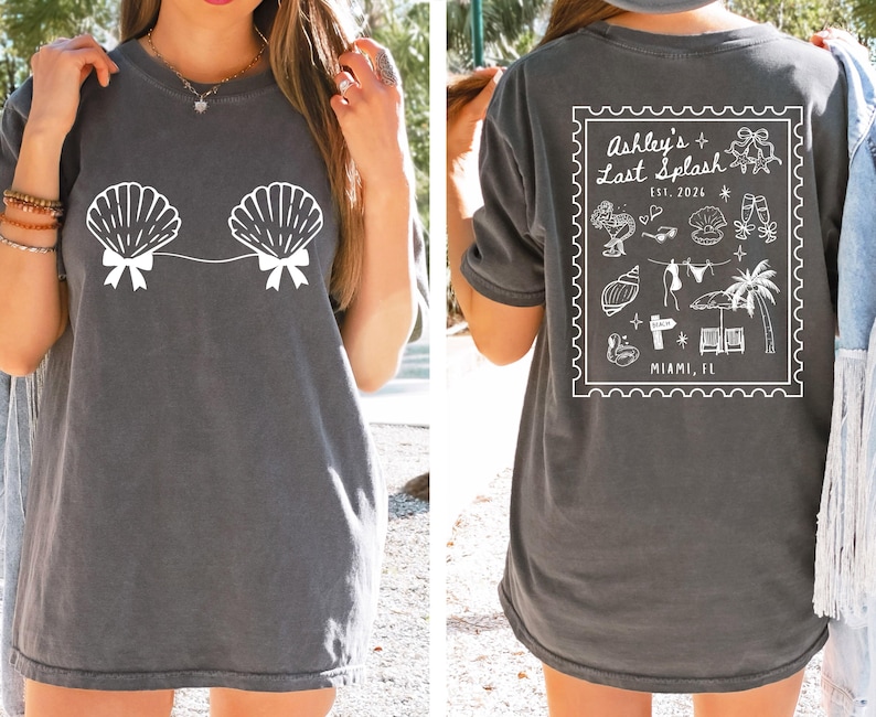 May include: Dark gray t-shirt featuring a white seashell design on the front. The back of the shirt has a white graphic with the text "Ashley's Last Splash" and various beach-themed illustrations. The text "Miami, FL" is also included.