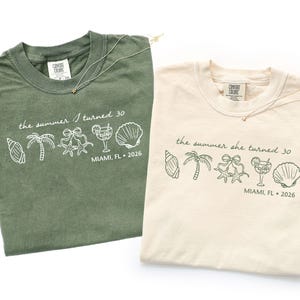 May include: Two t-shirts, one olive green and one cream, with the text "the summer I turned 30" and "the summer she turned 30" printed on them. The shirts also feature line art of seashells, palm trees, and cocktails. The location and year "MIAMI, FL 2026" are also printed on the shirts.