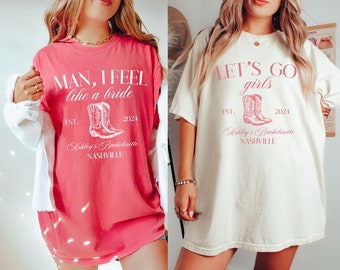 Op de afbeelding: Twee roze en witte T-shirts met een thema voor een vrijgezellenfeest. Het eerste shirt zegt "MAN, I FEEL like a bride" met een paar roze cowboylaarzen en de tekst "EST. 2024 Ashley's Bachelorette NASHVILLE". Het tweede shirt zegt "LET'S GO girls" met een paar roze cowboylaarzen en de tekst "EST. 2024 Ashley's Bachelorette NASHVILLE".