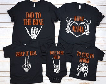 May include: Black Halloween-themed t-shirts with orange text and skeleton graphics. Designs include "Dad to the Bone," "Haunt Mama," "Creep It Real," "Bone to be Wild," and "To Cute to Spook."
