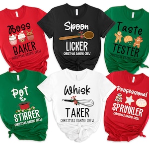 May include: Six Christmas baking crew t-shirts in various colours. Each shirt has a different baking-related title, including "Boss Baker" and "Spoon Licker", with festive graphics and the text "Christmas Baking Crew". The shirts are in red, black, white, and green.