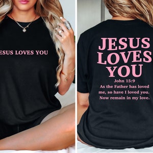 May include: Black t-shirt with the text "JESUS LOVES YOU" in pink on the front and the same text in pink with a Bible verse on the back.