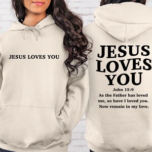 May include: A cream-colored hoodie with the text "JESUS LOVES YOU" on the front and the text "JESUS LOVES YOU" with the Bible verse "John 15:9 As the Father has loved me, so have I loved you. Now remain in my love." on the back.