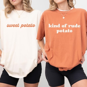 Puede incluir: Dos camisetas holgadas, una crema con "sweet potato" en escritura naranja, y la otra naranja quemado con "kind of rude potato" en letras blancas. Ambas se combinan con pantalones cortos negros.