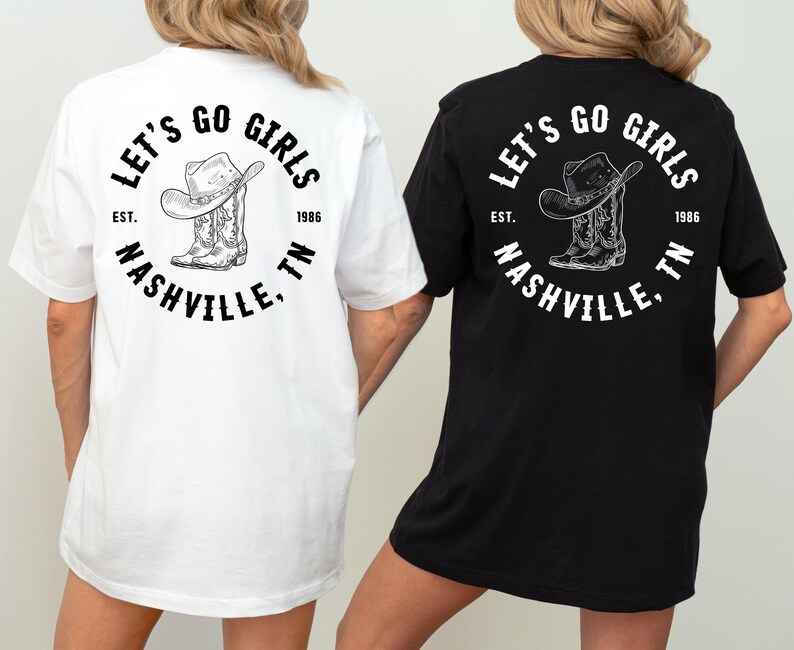 May include: White and black t-shirts featuring a circular graphic with the text "LET'S GO GIRLS", "NASHVILLE, TN", and "EST. 1986". The graphic includes a cowboy hat and boots. The shirts are short-sleeved.