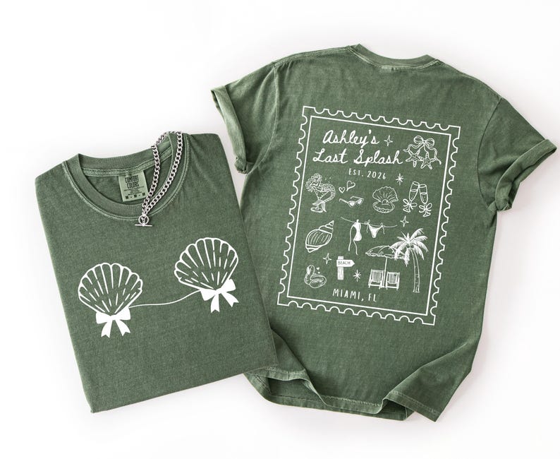 May include: Two olive green t-shirts with white graphics. One shirt features seashell designs with bows, and a silver chain necklace. The other shirt has a stamp-like design with text that reads "Ashley's Last Splash" and "Miami, FL".