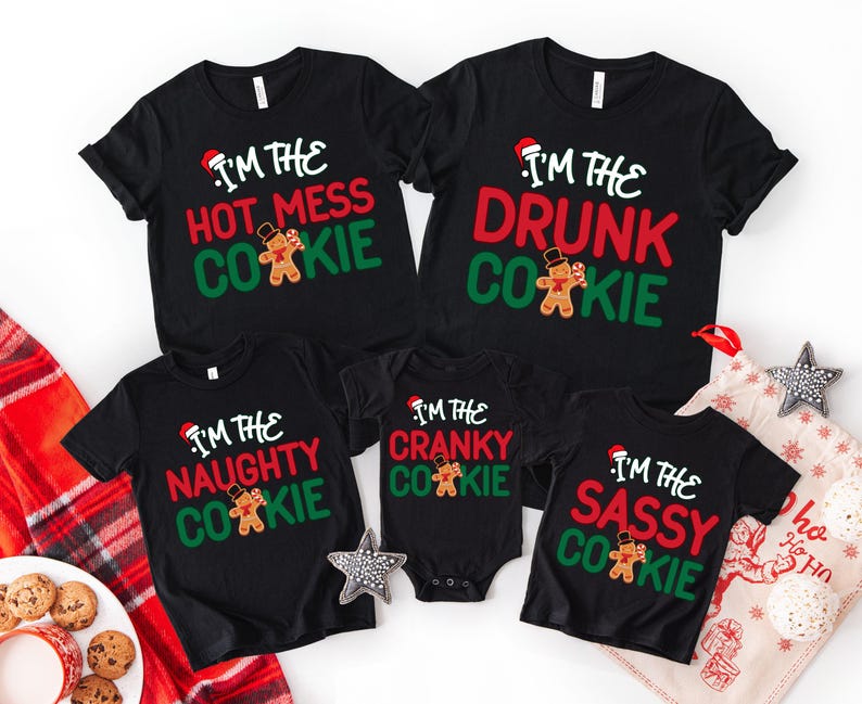 May include: A collection of black Christmas-themed t-shirts and a onesie. Each shirt features the phrase "I'm the" followed by a different adjective and "Cookie", along with a gingerbread man graphic and a Santa hat. The phrases include "Hot Mess", "Drunk", "Naughty", "Cranky", and "Sassy".