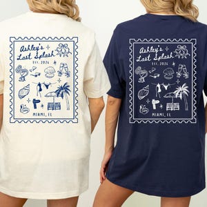 May include: Two t-shirts, one cream and one navy blue, featuring a stamp-like design on the back. The design includes the text "Ashley's Last Splash Est. 2026" and beach-themed illustrations. The bottom of the stamp reads "Miami, FL".