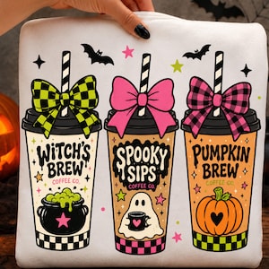 Puede incluir: Una sudadera blanca con un gráfico de tres tazas de café con pajitas y lazos. Las tazas están etiquetadas como Witch's Brew, Spooky Sips y Pumpkin Brew. El diseño incluye ilustraciones de un caldero, un fantasma y una calabaza con estrellas.