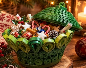 Puede incluir: Un cuenco de papel enrollado verde con tapa a juego, lleno de variados dulces navideños que incluyen bastones de caramelo, galletas en forma de estrella, pequeños adornos, piñas y dulces envueltos, creando un conjunto festivo.