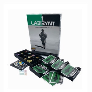 Può includere: Un gioco da tavolo chiamato "Labirynt" con una scatola verde e nera che mostra un soldato che cammina. Il gioco tratta della guerra al terrorismo dal 2001 ad oggi. La scatola è aperta e mostra i pezzi del gioco, tra cui carte e dadi.