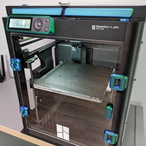 K&ouml;nnte beinhalten: Ein schwarzer 3D-Drucker mit einer Glast&uuml;r und einem gr&uuml;nen Bedienfeld. Der Drucker hat eine transparente Kunststoff-Baustelle und einen blauen Lichtstreifen oben. Der Drucker ist mit "Bambu Lab P1P" beschriftet.