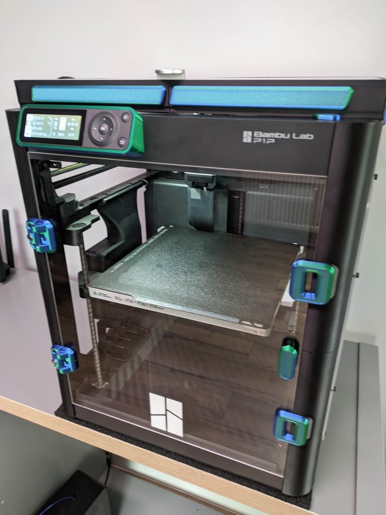 K&ouml;nnte beinhalten: Ein schwarzer 3D-Drucker mit einer Glast&uuml;r und einem gr&uuml;nen Bedienfeld. Der Drucker hat eine transparente Kunststoff-Baustelle und einen blauen Lichtstreifen oben. Der Drucker ist mit "Bambu Lab P1P" beschriftet.