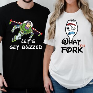 May include: Two t-shirts with a Toy Story theme. The black t-shirt features Buzz Lightyear with the text "Let's Get Buzzed". The white t-shirt features Forky with the text "What the Fork".