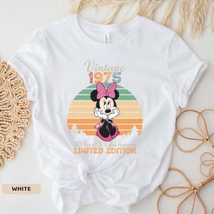 May include: White t-shirt with a vintage 1975 design featuring a cartoon image of Minnie Mouse in front of a sunset. The text "50 Years of Being Awesome Limited Edition" is printed below the image.